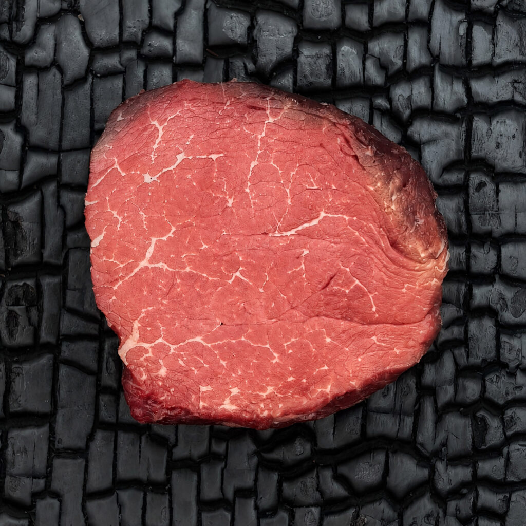 Rohes Filetsteak vom Rind mit feiner Marmorierung, rote Fleischfarbe, einzelnes Stück auf dunkler, verkohlter Holzoberfläche.