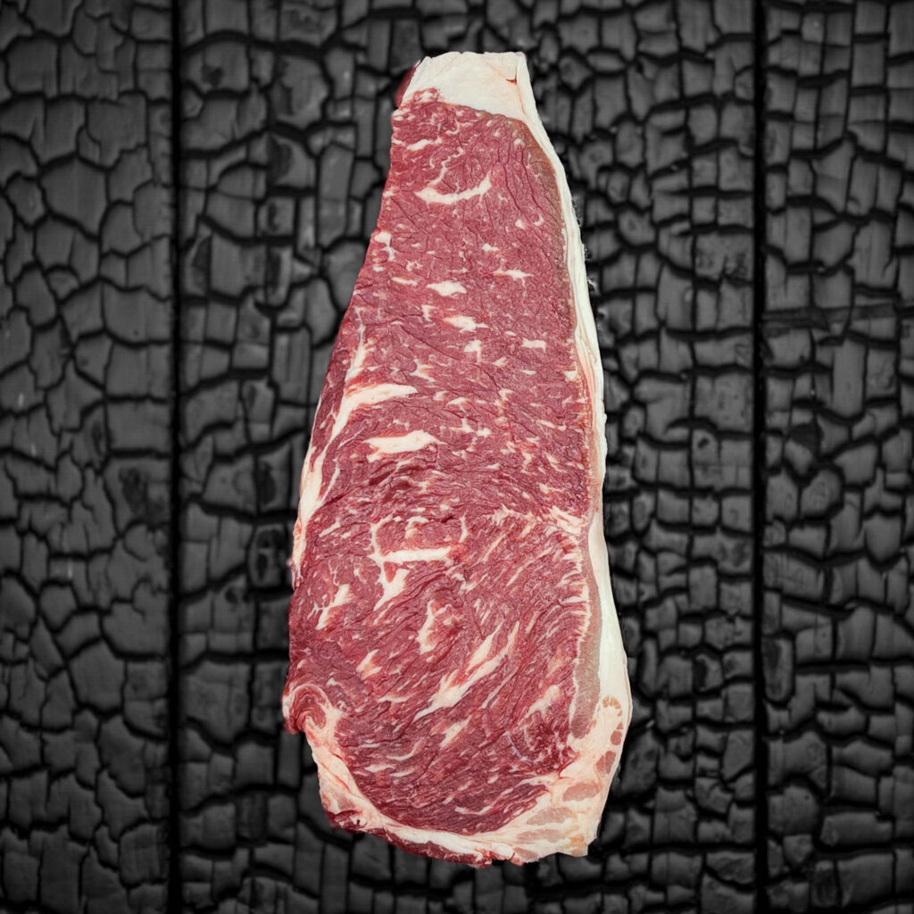 Rohes Striploin-Steak vom Rind mit guter Marmorierung, rote Farbe mit gleichmäßigem Fettrand, mittig auf dunkler, verkohlter Holzoberfläche.