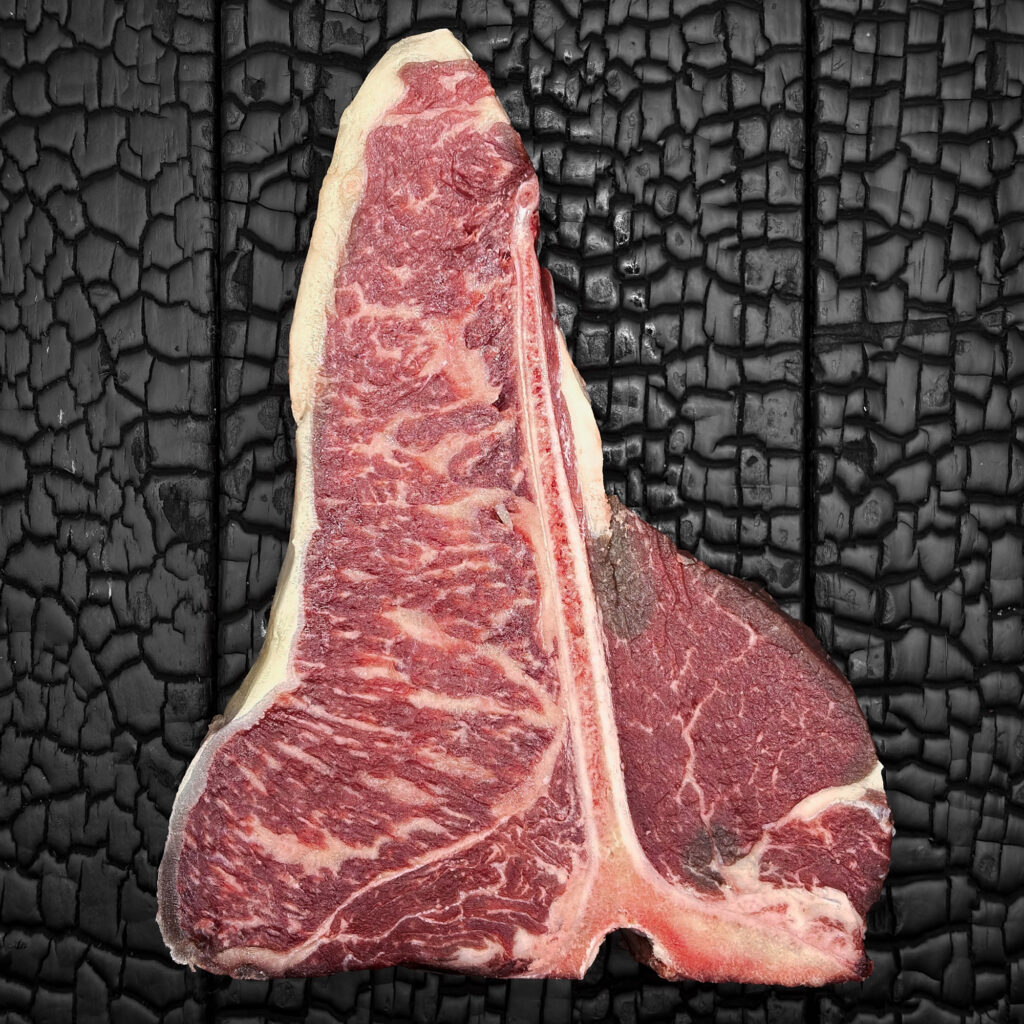 Rohes T-Bone-Steak vom Rind mit T-förmigem Knochen, gut marmoriert, Filet- und Beiriedanteil, rote Farbe mit hellem Fettrand, mittig auf dunkler, verkohlter Holzoberfläche.