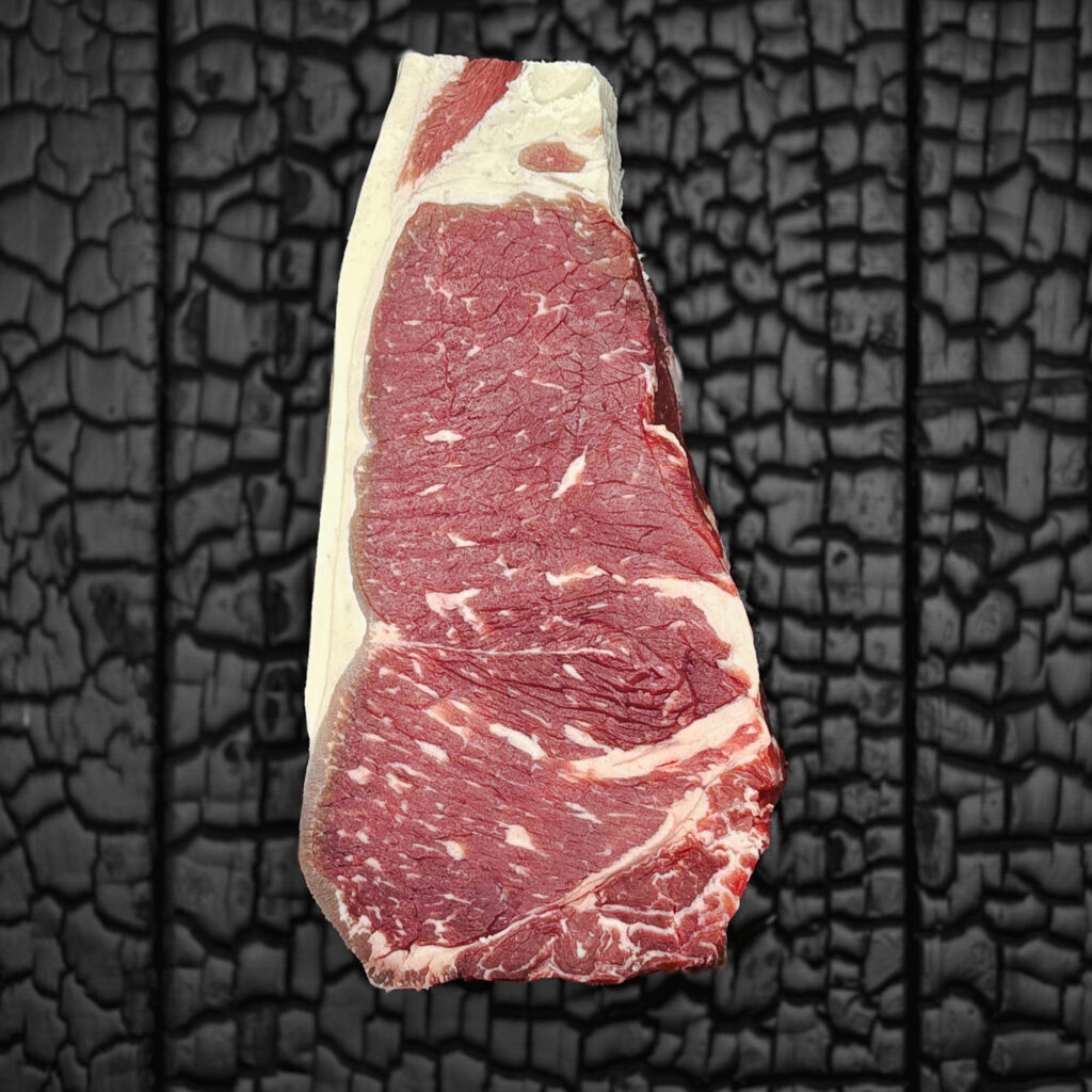 Rohes Striploin-Steak vom Rind mit feiner Marmorierung, rote Farbe mit gleichmäßigem Fettrand, mittig auf dunkler, verkohlter Holzoberfläche.
