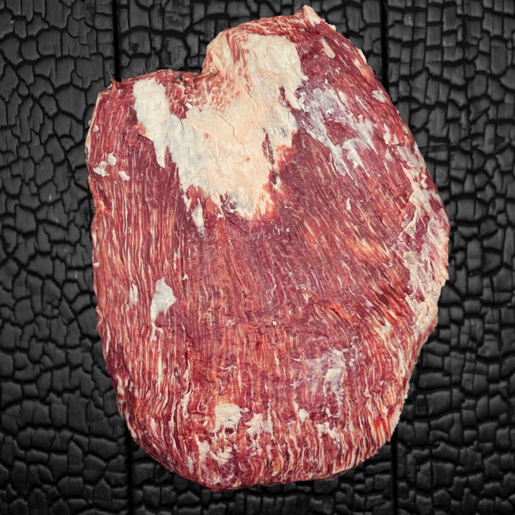 Rohes Flank-Steak vom Wagyu-Rind, stark marmoriert, rote Fleischfarbe mit sichtbarer Faserstruktur, mittig auf dunkler, verkohlter Holzoberfläche.