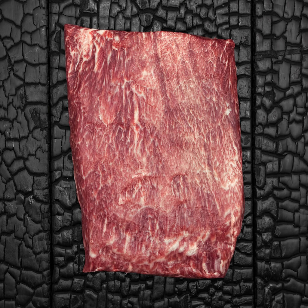 Rohes Flat-Iron-Steak vom Wagyu-Rind, halbiert, stark marmoriert, rote Fleischfarbe mit feiner Faserstruktur, rechteckige Form, mittig auf dunkler, verkohlter Holzoberfläche.