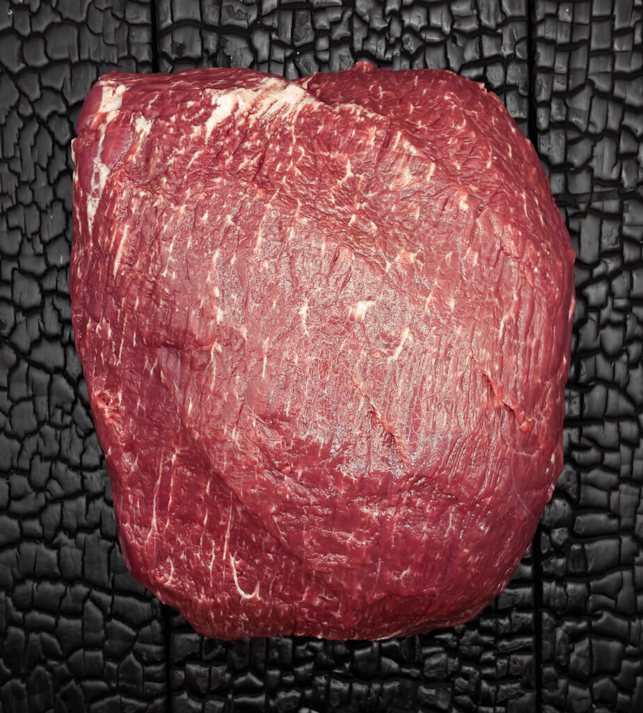 Ganzes rohes Sirloin vom Wagyu-Kreuzungsrind, kompakte Form, gut marmoriert, rote Farbe, auf dunkler, verkohlter Holzoberfläche.