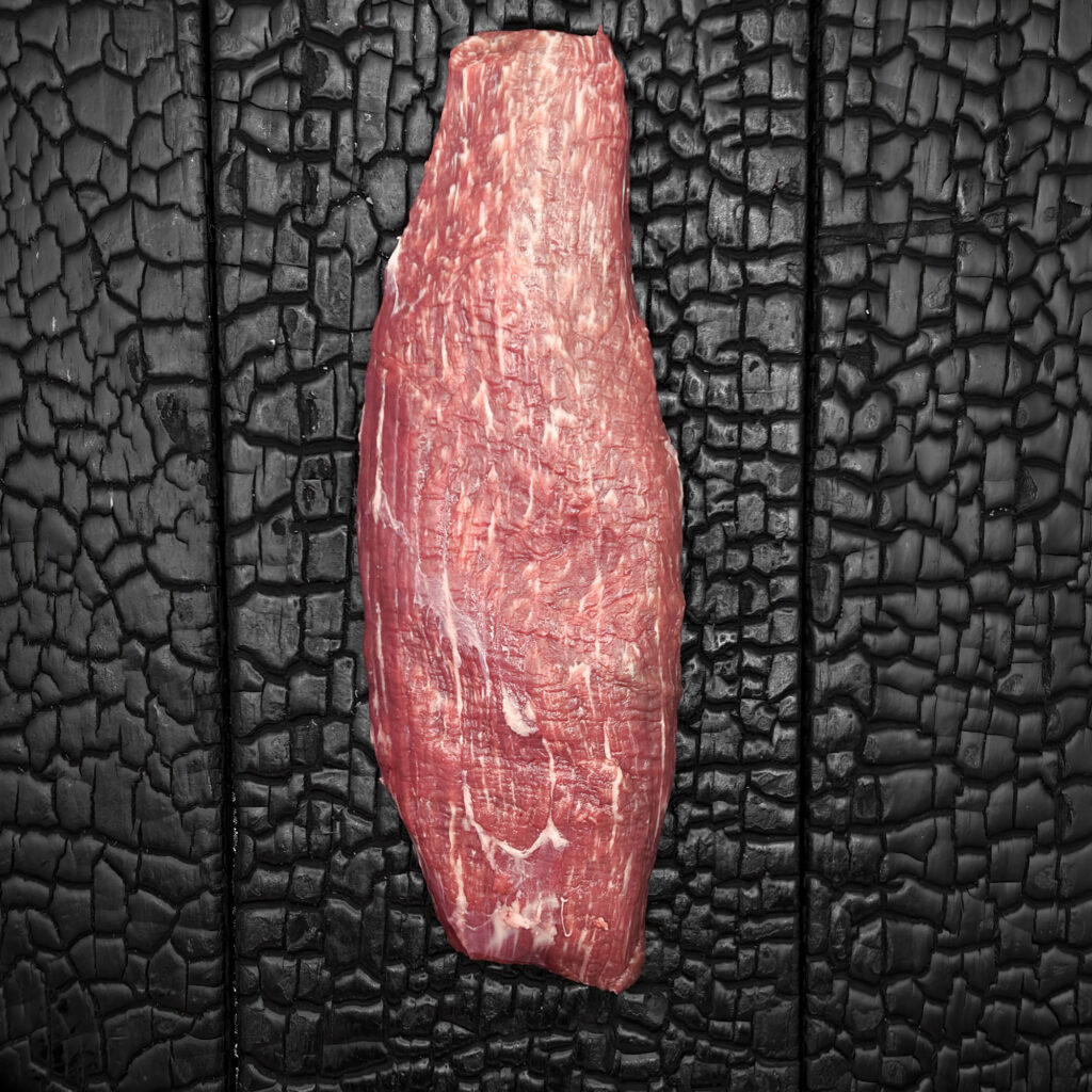 Rohes Teres-Major-Steak vom Wagyu-Kreuzungsrind, längliche Form, gut marmoriert, rote Farbe, mittig auf dunkler, verkohlter Holzoberfläche.