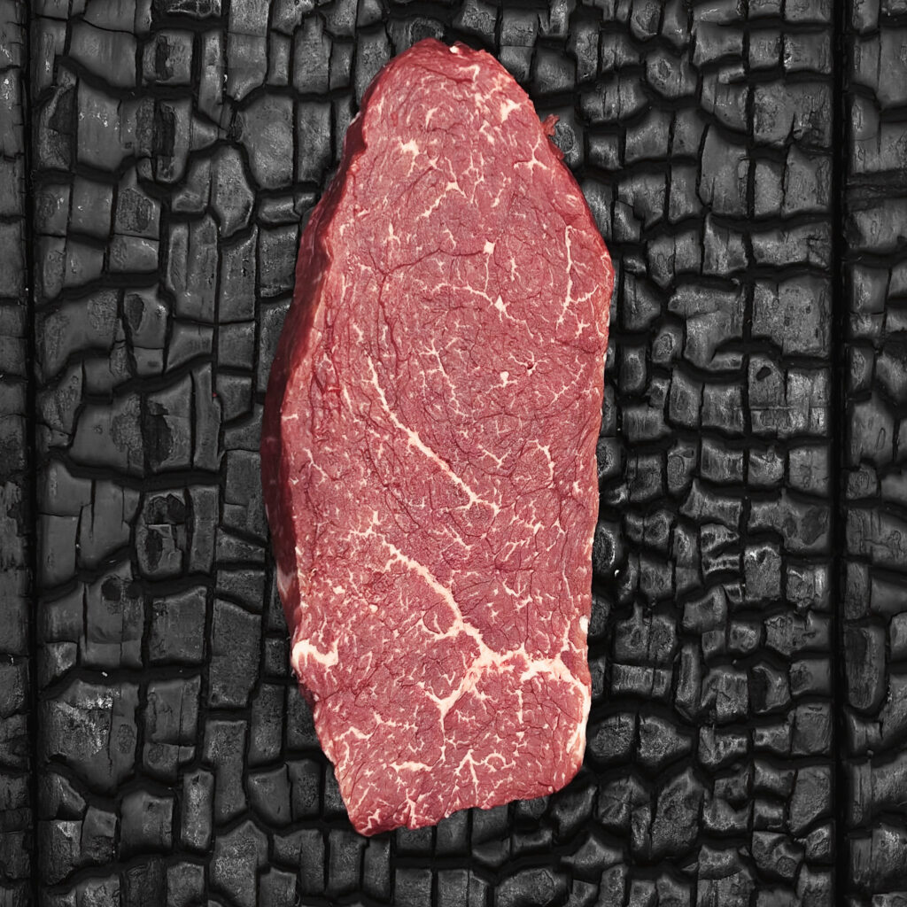 Rohes Sirloin-Steak vom Wagyu-Rind, gut marmoriert, rote Fleischfarbe mit feinen Fettadern, längliche Form, mittig auf dunkler, verkohlter Holzoberfläche.