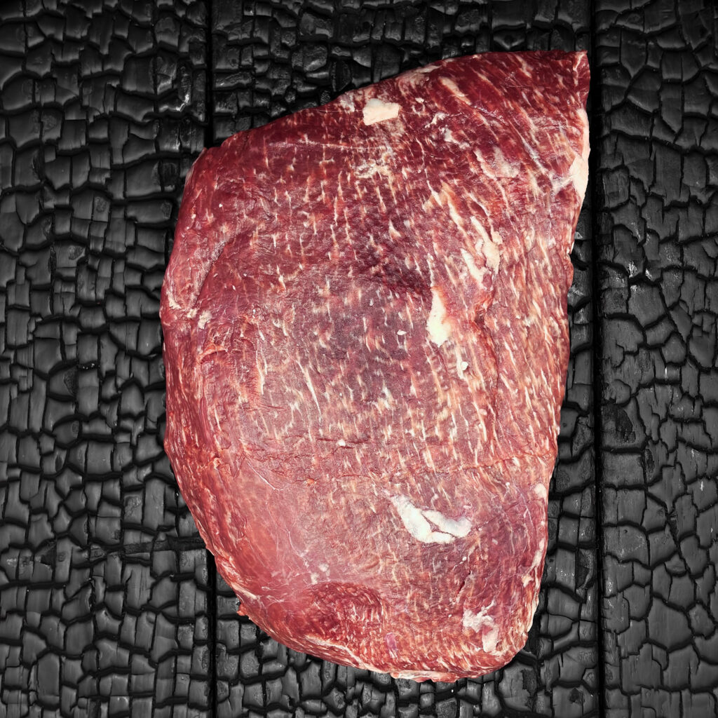 Rohes Sirloin im Ganzen vom Wagyu-Rind, gut marmoriert, rote Fleischfarbe mit feinen Fettadern, mittig auf dunkler, verkohlter Holzoberfläche.
